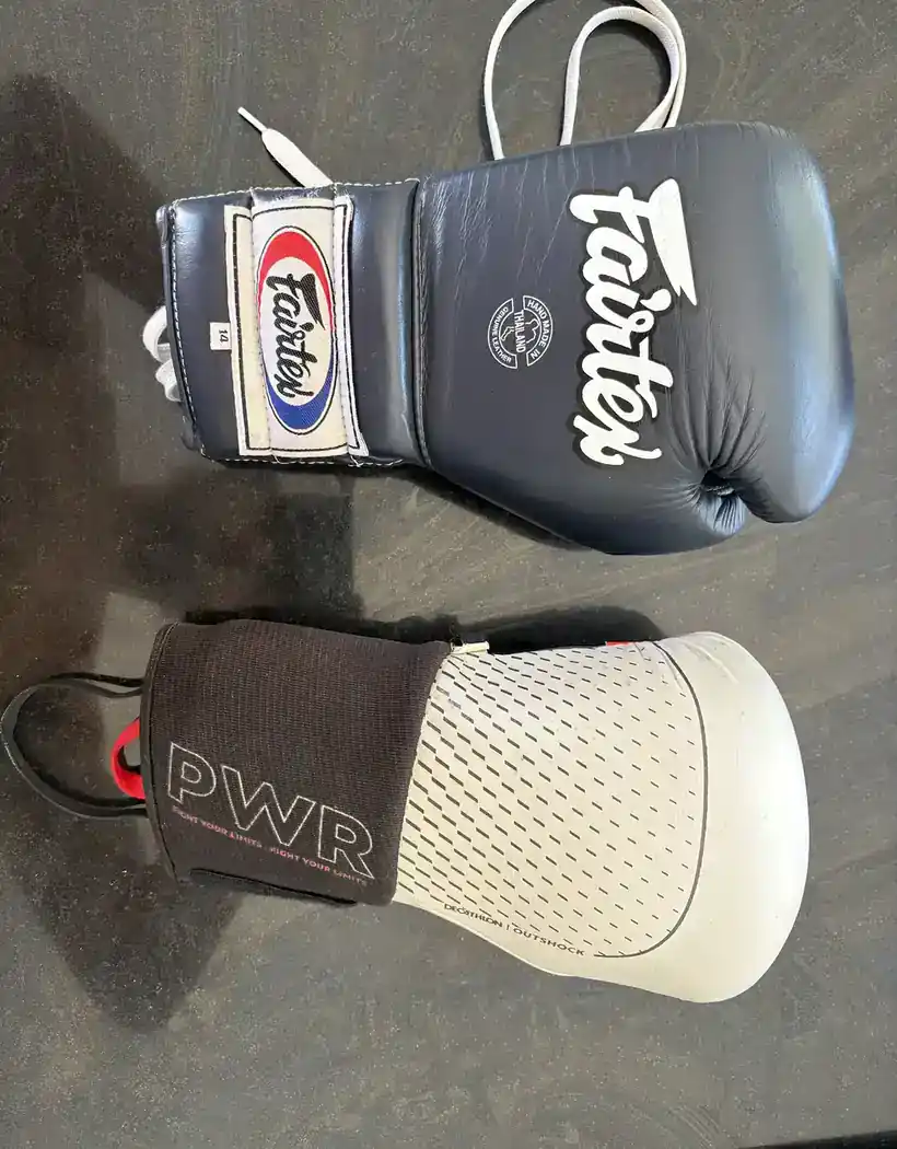 Gant de boxe Decathlon Outshock blanc pos&eacute; sous un Fairtex BGV7 bleu marine &agrave; la&ccedil;age, vus de dos
